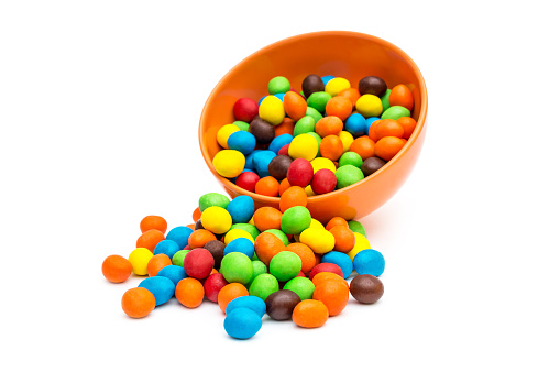 Sweet round candies scattered from bowl on white.