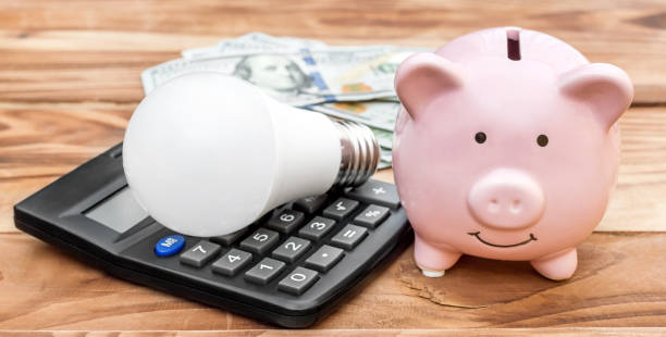 Piggy bank with light bulb, calculator and money on wooden background. Piggy bank with light bulb, calculator and money on wooden background. energy bill photos stock pictures, royalty-free photos & images
