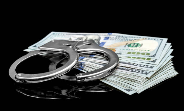 istock Dollar bills with handcuffs on black reflective background. 1048950406