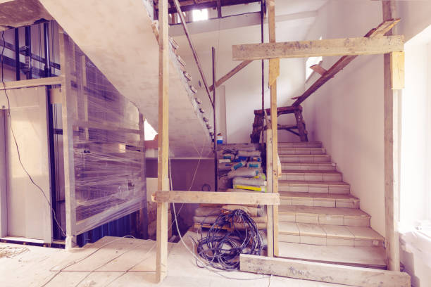 istock Construction materials, electrical wires, bags with cement, claircole  and putty, stairs with temporary wooden railing and elevator in an apartment is during on the construction, remodeling, overhaul, rebuilding and renovation 1048987990