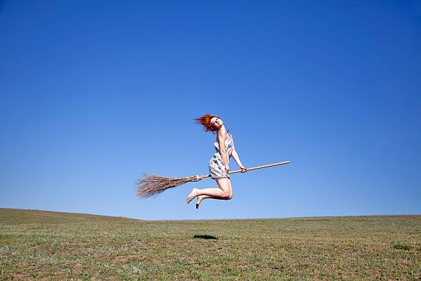 istock Young red-haired witch on broom flying over green grass field 104899044