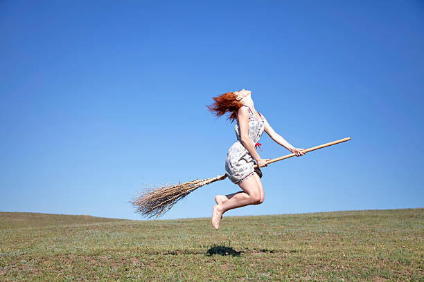 istock Young red-haired witch on broom flying over green grass field 104899094