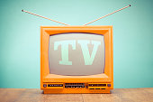 Retro old orange TV receiver on table front mint green wall background. Vintage style filtered photo