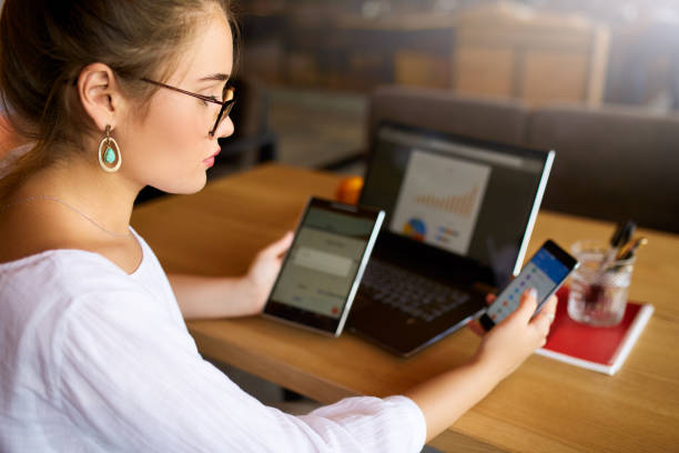istock Mixed race woman in glasses working with multiple electronic internet devices. Freelancer businesswoman has tablet and cellphone in hands and laptop on table with charts on screen. Multitasking theme 1049014096