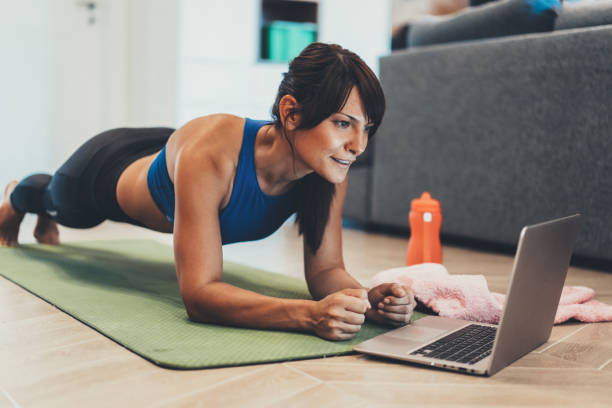 Sporty woman doing plank in front of her laptop Strong sporty woman is doing working out at home and doing plank in front of her laptop exercise room photos stock pictures, royalty-free photos & images
