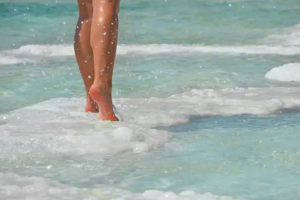 Photo of Female feet with manicure on stone, covered with salt formations between the waves in the water. Crystallization of salt on stone, spa, therapy in the Dead Sea, Israel