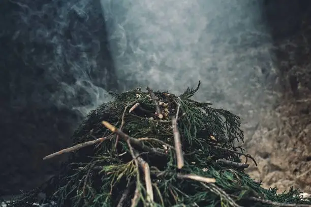 Photo of a pile of pine branch smoking on the holy sacred fire with a ray of sun peaking in from the top