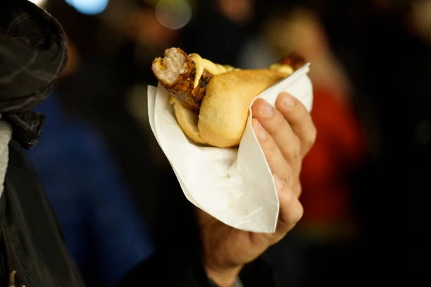 Hand holding a Bratwurst with mustard by night stock photo