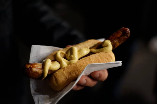 Hand holding a Bratwurst with mustard by night stock photo