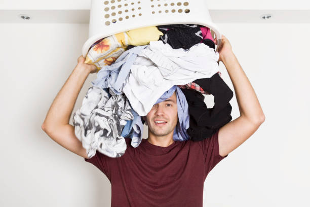 Worried and crying young men before laundry. He has enough housekeeping Frustrated young man with full of clothes on his head. Laundry time laundry husband housework men stock pictures, royalty-free photos & images