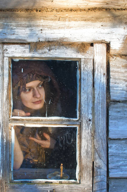 retrato de uma mulher de camponês envolvida em um xale de lã, que olha pela janela de uma casa de vila velha - witch smiling evil bizarre - fotografias e filmes do acervo