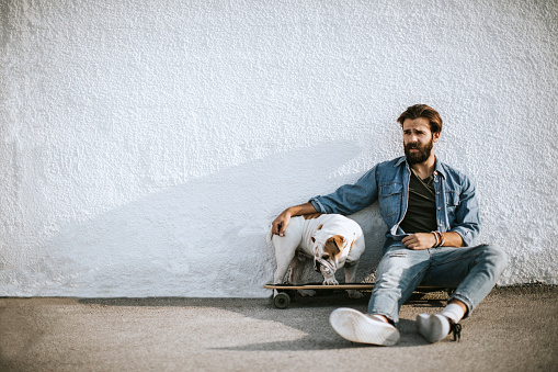 Young Man Resting On Skate Leaning on Wall Accompanied By His Bulldog