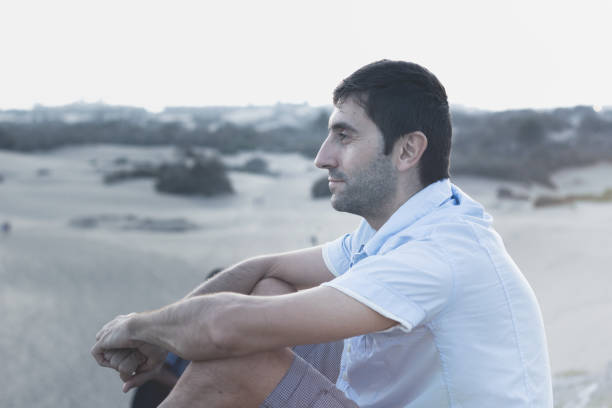 istock Thoughtful man sitting on Maspalomas sand dunes at sunset 1049094228