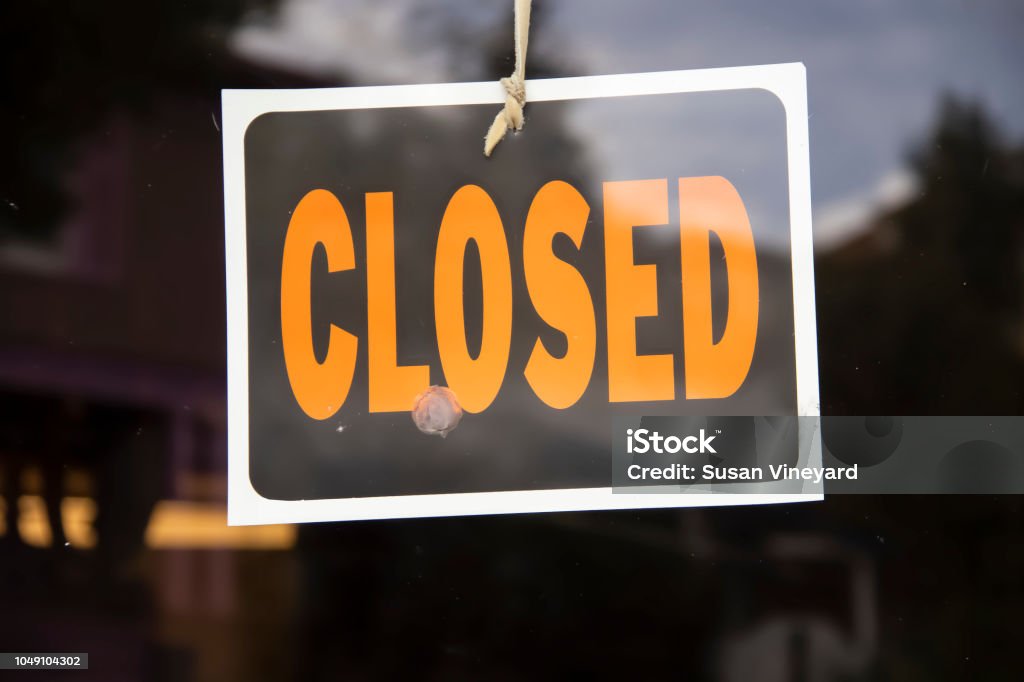 Closed sign hanging in business window by a string - crooked with glob of glue also attaching it to window - some abstract reflections Closing Stock Photo