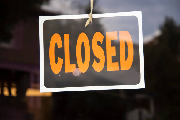 Closed sign hanging in business window by a string - crooked with glob of glue also attaching it to window - some abstract reflections stock photo
