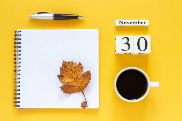 calendar November 30 cup of coffee, notepad with pen and yellow leaf on yellow background stock photo