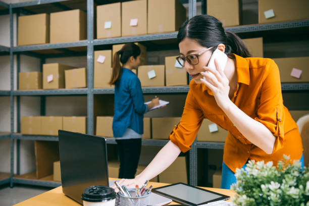 manager calling client to confirm the goods manager in the e-shop company is calling client to confirm the goods they've ordered, and the other staff is counting the goods in the background warehouse office stock pictures, royalty-free photos & images