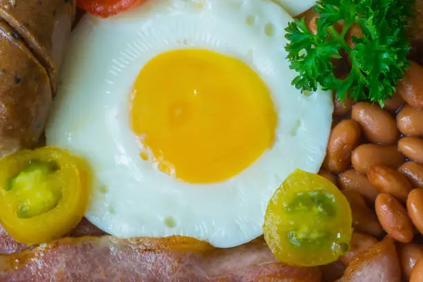 Close up of delicious fried egg with beans and meat on the table. British breakfast concept