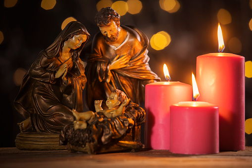 Christmas nativity scene of baby Jesus on the manger with burning candles and blurred sparkling light background