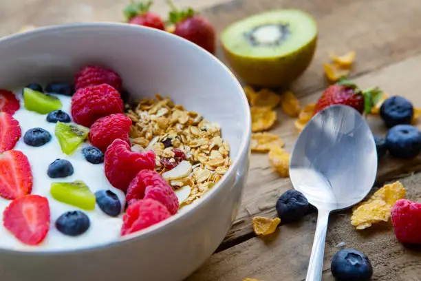 Closeup of tasty cereals with fresh fruits and yogurt in a bowl. Shot on the wooden table