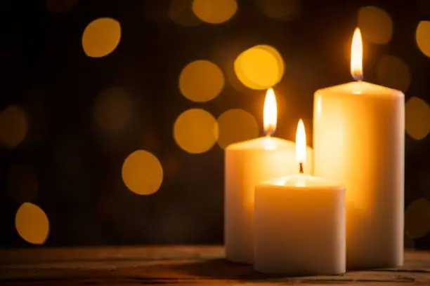 Close up of three burning candles on the wooden table with blurred Christmas light background