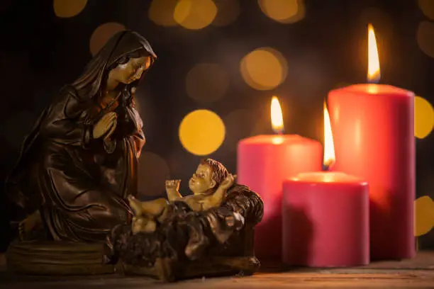 Statuette of baby Jesus with Mary and burning candles on the table with blurred sparkling light background