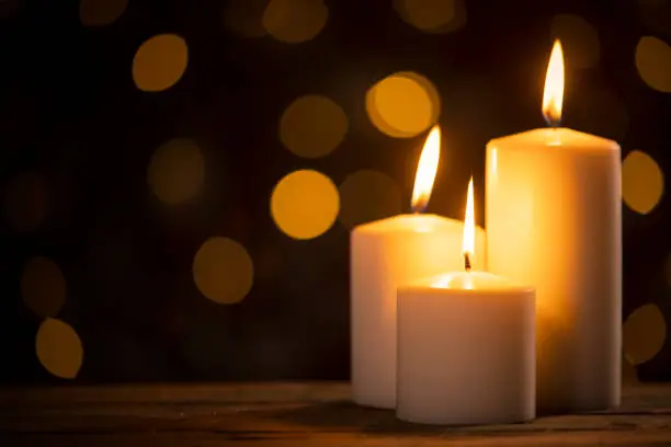 Close up of white burning candles on the table with golden light background blur