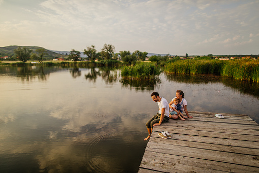 Photo of a young loving family who enjoys summer afternoon on a dock by the lake