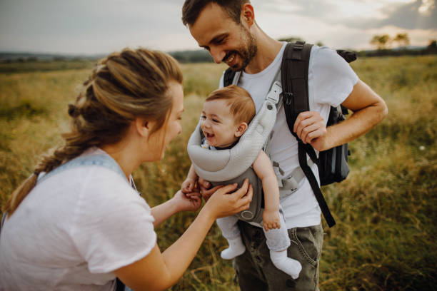 Young family spending time outdoors Photo of a young loving family who enjoys spending their time together, outdoors with their baby who is in a baby carrier baby carrier stock pictures, royalty-free photos & images