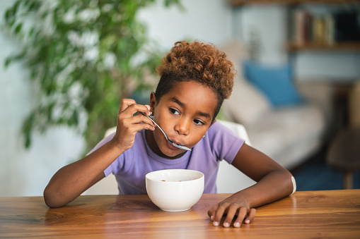 Cute African girl is having cereal breakfast at home.