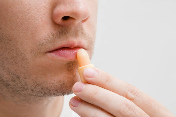 istock Handsome, young, bearded man using natural lips balm on light gray background. Care about healthy, moisture and soft lips. Protection from cold winter, hot summer and windy autumn time. 1049213518