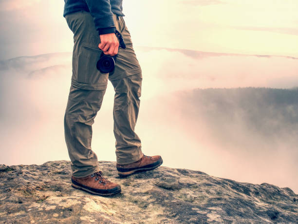 Tourist with camera in hand stays in trekking trousers and brown boots. stock photo
