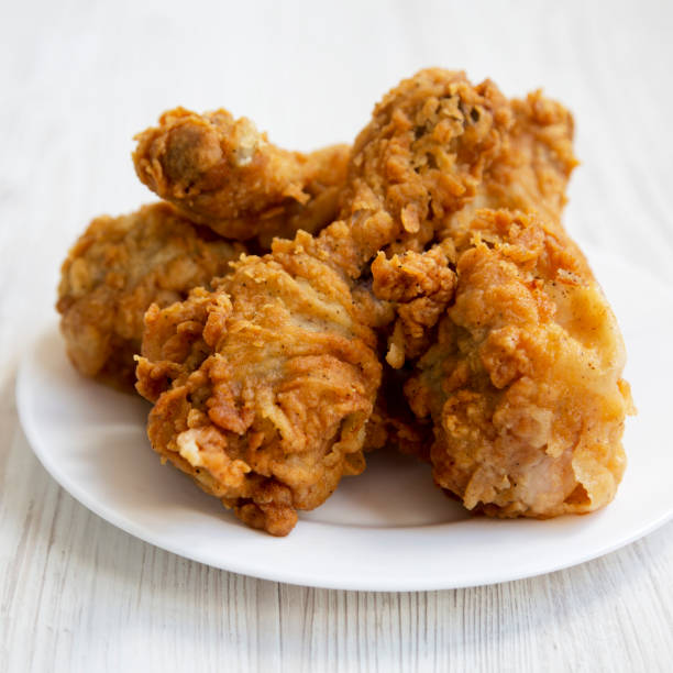 istock Fried chicken drumsticks on a white round plate over white wooden background, close-up. Side view. 1049214234