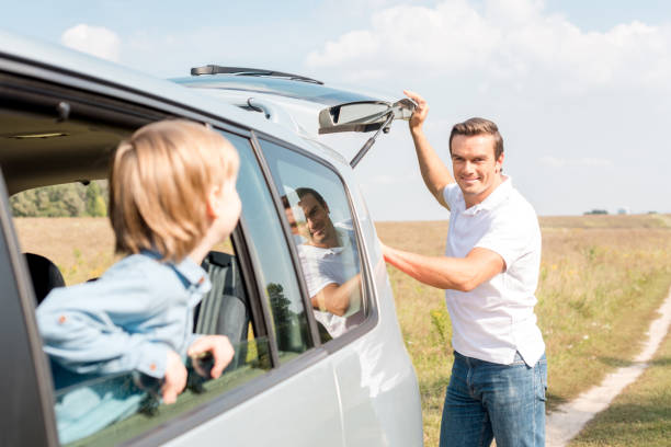 istock little son looking at father out window while he opening car trunk in field 1049237614