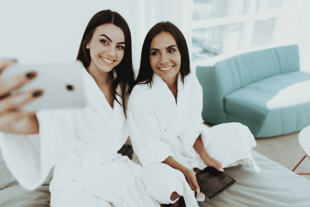istock Girls In A Bathrobes Are Doing A Selfie On A Bed. 1049248626