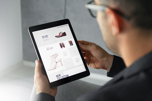 Male hand is browsing an online shop which is selling shoes on digital tablet.