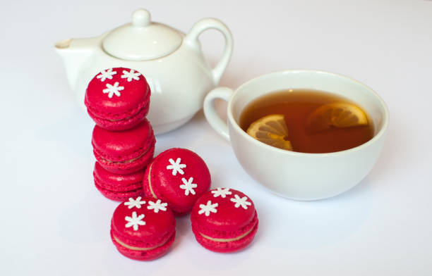 Cup of tea with french macaroon on white background. Tea pot, cup of tea, lemon and  pink macaroon lying on white background. Christmas macaroons with snowflake.