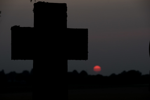 Cross in silhouette with sinking red sun