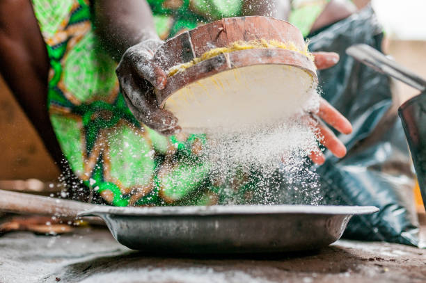 beautiful image of black woman hands searching and sifting corn white flour while cooking traditional african dish with african dress stock photo