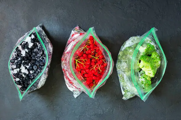 Photo of Frozen berries and vegetables in bags in packages on dark concrete background - close up