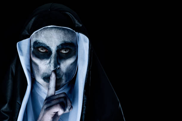 frightening evil nun asking for silence closeup of a frightening evil nun, wearing a typical black and white habit, asking for silence, against a black background with a blank space on the right angry nun stock pictures, royalty-free photos & images