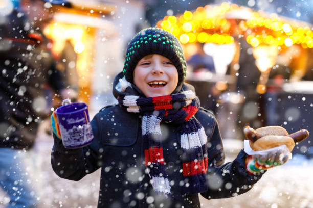 little cute kid boy eating german sausage and drinking hot children punch on christmas market - hot chocolate hot drink heat drinking imagens e fotografias de stock