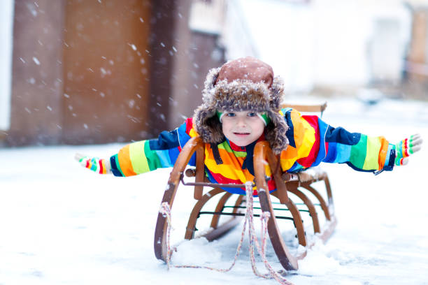 kleines kind junge genießen schlittenfahrt bei schneefall. glückliches vorschule kind auf vintage schlitten fahren. - little boys sled clothing slide stock-fotos und bilder