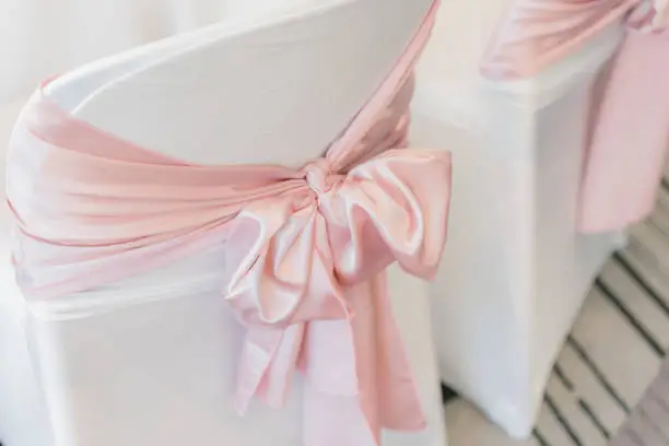 White chair covers with pink satin silk sash bow. Wedding, event, reception.