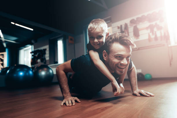 istock Man Is Doing Push Ups In Gym With Son On A Back. 1049284288