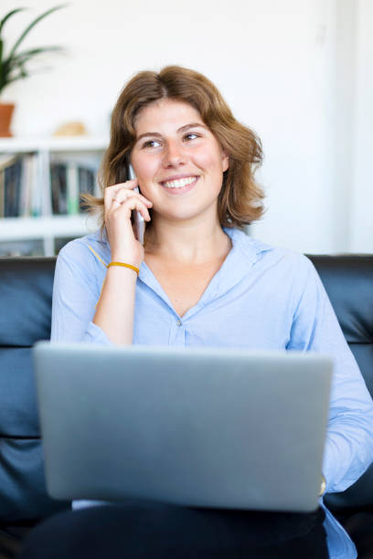 istock Smiling woman sitting on a sofa at home using a laptop 1049288632