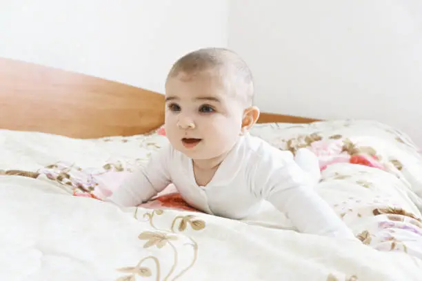 Cute caucasian baby on the bed looking sideways. Horizontal shot