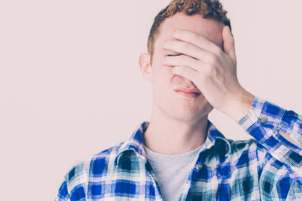 Annoyed Young Caucasian Man Covering Eyes with Hand Annoyed red haired Caucasian guy covering eyes with hand. Young man suffering from headache. Upset student making face palm gesture. Do not want to see or head ache concept hair covering eyes stock pictures, royalty-free photos & images