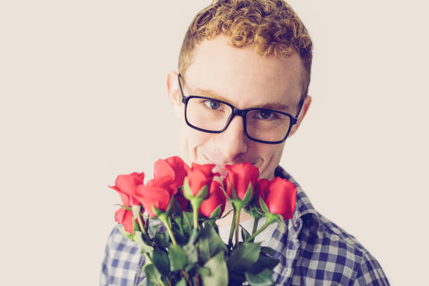 Smiling red haired Caucasian guy with bunch of red roses. Shy young man posing with flowers for special day. Romance or celebration concept