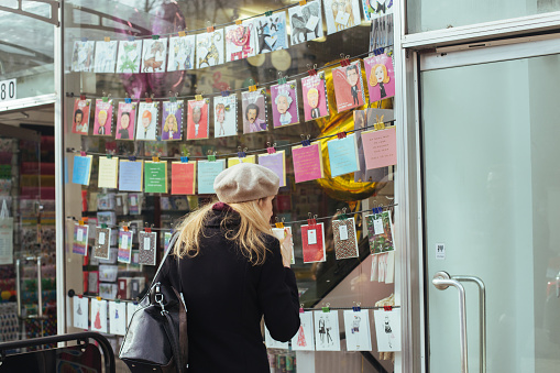 London / UK - March 11, 2018: woman is looking through the window of Card Bureau which is a Card & Poster Shop located on the Holland Park Avenue in London, UK